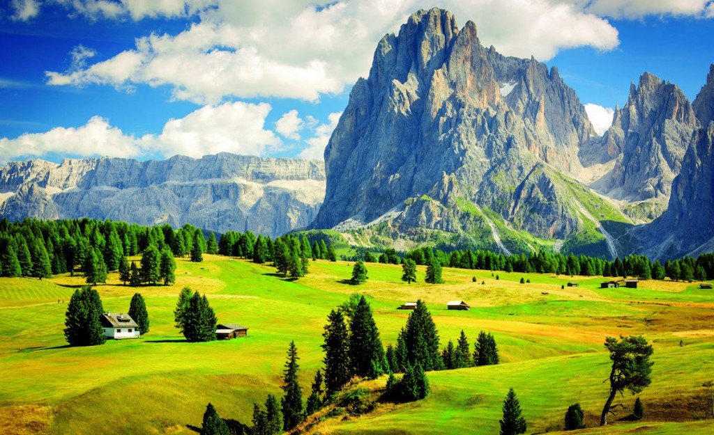Verdant green pasture with very tall, steep rocky dolomite in the background.