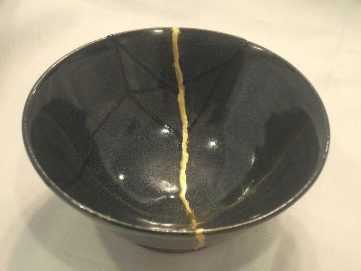 Black ceramic bowl broken in two. Crack has been repaired with gold-colored resin. (The gold resin accentuates the crack).