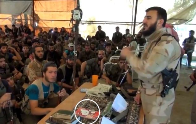 Zahran Alloush giving press conference in military fatigues, with Hello Kitty notebook on table in front of him.